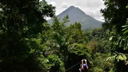 A student ziplining through a dense green forest, with a distant volcano in the background under a partly cloudy sky—an unforgettable adventure perfect for any school travel program by Global Works.