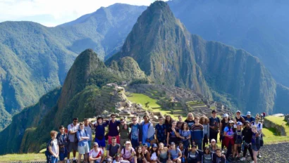 A dozen people standing side by side with their backs towards the camera facing a mountain range with a sunny sky above||||||||||||