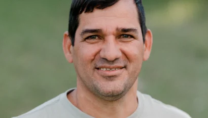A man with short dark hair stands outdoors wearing a gray t-shirt with "A. EAGLE USA" on the front, smiling at the camera.