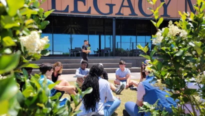 A group of student travelers sit in a circle on the grass on a student school group travel program gathering.