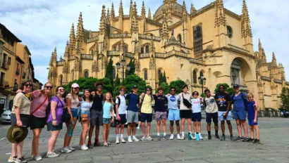 A group of people on a Spain school trip poses in front of a large, ornate historic cathedral with spires and arches on a sunny day.