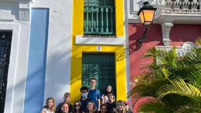 A group of student travelers posing for a photo in front of a colorful building during their school trip to Puerto Rico.