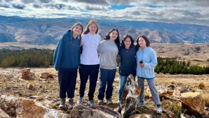 Five people stand together on rocky ground with mountains and a cloudy sky in the background, capturing a memorable moment from their Peru school trip.