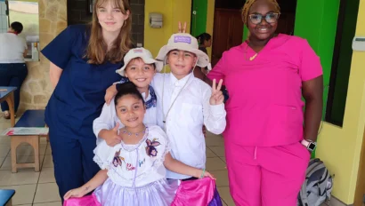 Two adults in scrubs and three children in colorful costumes pose together indoors.