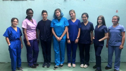 A group of eight people standing in scrubs against a light blue wall.