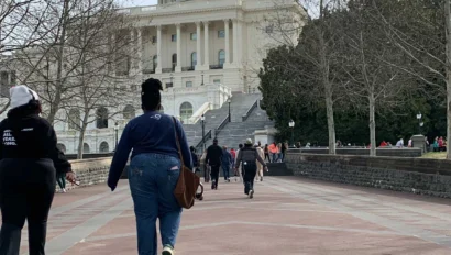 People participating in an American history travel program walk toward the United States Capitol building on a cloudy day, surrounded by leafless trees.