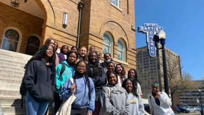 A group of teenagers poses for a photo on the steps outside a brick building with a sign reading "16th St Baptist Church," capturing an unforgettable moment during their american history travel experience.