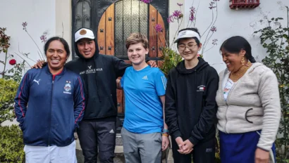 Five people stand together smiling in front of a house doorway, with plants and flowers on either side, celebrating the start of their language immersion trip.