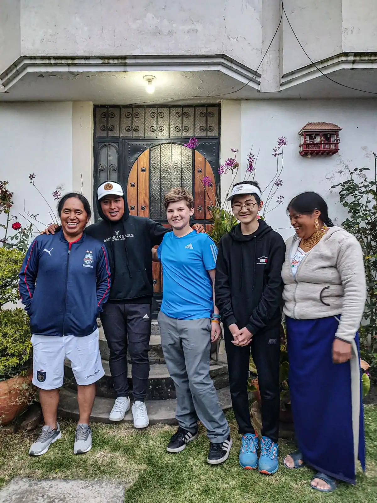 Five people stand together smiling in front of a house doorway, with plants and flowers on either side, celebrating the start of their language immersion trip.