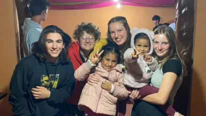 A group of people, including three adults and three children, pose and smile for a photo indoors with wooden pillars and warm lighting.