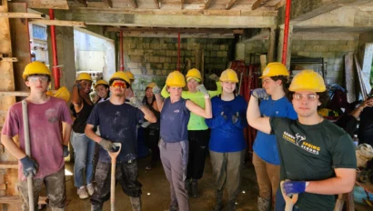 Group of construction workers wearing hard hats and safety glasses, posing inside a building under construction, with tools in hand.