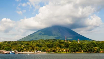 A lush green island with a volcano partially covered by clouds, surrounded by water. Boats are docked along the shore.