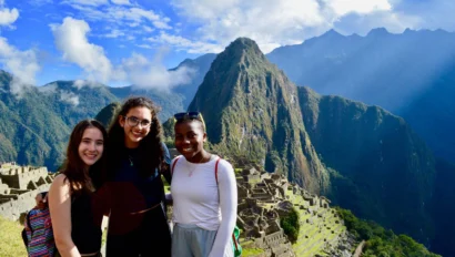 Three people smiling at Machu Picchu, with mountains and ruins in the background.