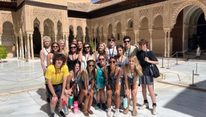 A group of people posing for a photo in a sunny courtyard with intricate architectural details in the background.