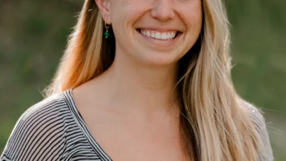 A woman with long blonde hair wearing a striped shirt smiles outdoors.