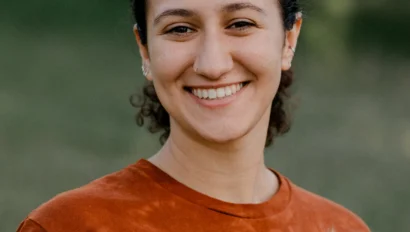 A person smiling outdoors, wearing a brown T-shirt with a fox design.