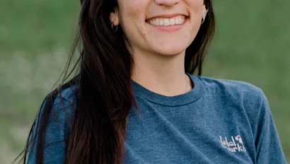 Woman smiling in a green outdoor setting, wearing a blue t-shirt.