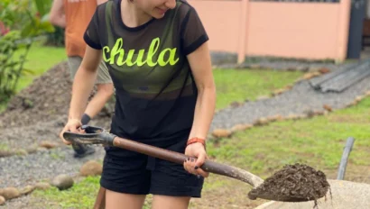 Person shoveling dirt into a wheelbarrow in a garden setting.
