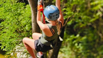 A person wearing a helmet and harness rides a zip line through a wooded area during an adventurous Fiji school trip.