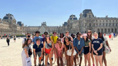 A group of young people poses for a photo outside the Louvre Museum in Paris on a sunny day, capturing memories from their France school trip with the historic building visible in the background.