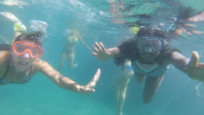 Four people on a Dominican Republic school trip snorkeling underwater, wearing masks and snorkels, with arms extended forward in clear blue-green water.