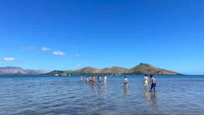 People walking in shallow water toward an island under a clear blue sky.
