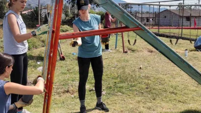 Three people repairing a slide in an outdoor park. Various tools and water bottles are on the grass nearby.