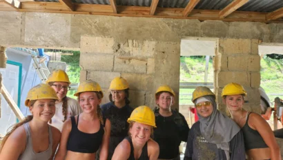 A group of eight people wearing yellow hard hats and casual work clothes stand together in a partially constructed building.