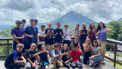A group of young people pose on a wooden deck with a mountain and cloudy sky in the background.
