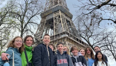 A group of people stands in front of the Eiffel Tower, with bare trees in the background. Some are holding bags and water bottles.