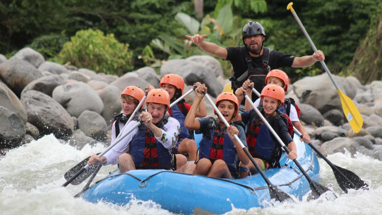 Group of eight people in helmets and life jackets rafting on a river.
