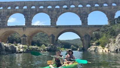 Two people kayaking on a calm river with the Pont du Gard Roman aqueduct in the background under a clear blue sky—a perfect scene from a student trip to France.