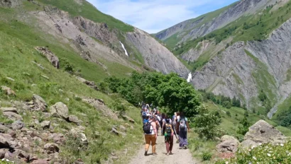 A group of people hiking on a dirt path through a mountainous landscape under a clear blue sky.