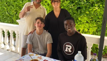 Four people pose and smile by a table set with food, drinks, and plates on a covered patio with greenery in the background during their language immersion trip.