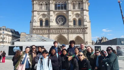 Group of people posing in front of the Notre-Dame Cathedral in Paris on a sunny day. Construction cranes are visible in the background.