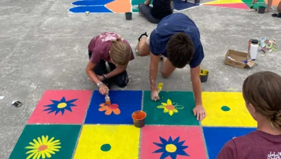 People painting colorful geometric patterns on a concrete surface outdoors.