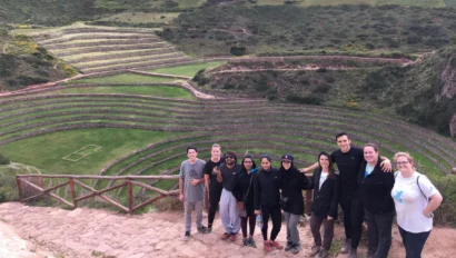 A group of people stand on a stone path with agricultural terraces and green fields in the background.