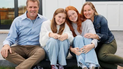 A family of four sits together on a porch step, smiling at the camera.