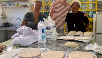 Three people stand in a kitchen behind a counter with dough rounds on baking sheets, preparing bread during their Spanish immersion program.