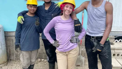 Four students wearing hard hats, gloves, and boots stand together outside a building, posing and smiling for the camera during a teen service trip to Puerto Rico.