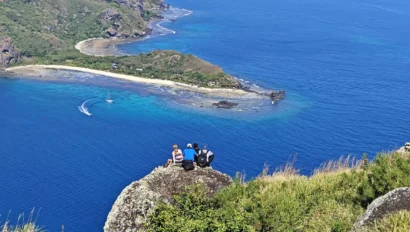 three people sitting on the ground overlooking the water.