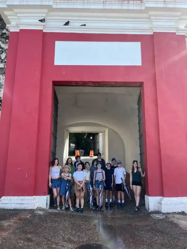 A group of people stands in front of a large red and white arched gate, posing for a photo on a sunny day.